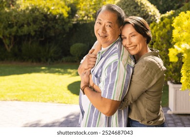 A couple, smiling middle-aged woman hugging asian man outdoors in sunny garden, enjoying family time. happiness, bonding, multigenerational, sunshine, joyful, relationship - Powered by Shutterstock