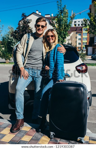 couple of smiling tourists with baggage near car\
on street