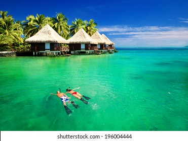 Couple Snorkling In Tropical Lagoon With Over Water Bungalows