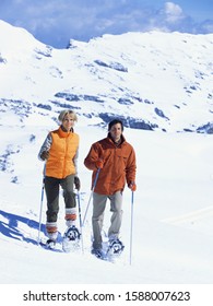 Couple Snowshoeing Downhill With Ski Poles