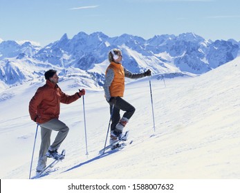 Couple Snowshoeing Uphill With Ski Poles