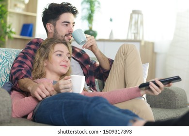 Couple Snuggling On Sofa With Cup Of Tea Watching Tv