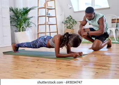 Couple in sporty athletic clothing exercising, woman planking man encouraging high five when she finishes completes training set