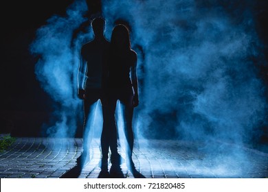 The couple stand on the dark alley on the blue fume background. night time