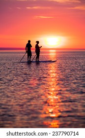 Couple Stand Up Paddle Boarding At Sunset