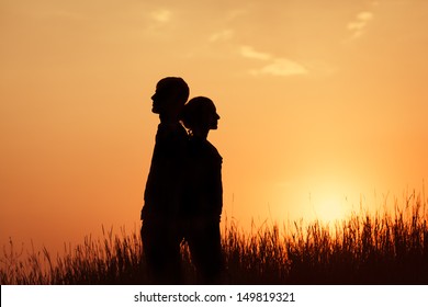 Couple Standing Against The Sunset Back To Back