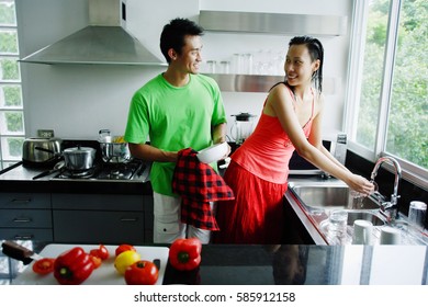 Couple Standing In Kitchen, Woman Washing Hands, Man Drying Dishes