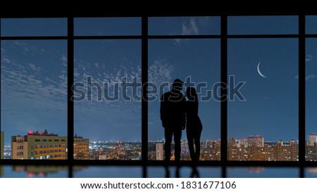 The couple standing near the panoramic window on a city moon background