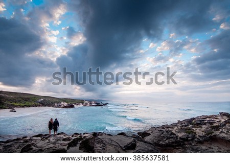 A couple standing at the ocean edge of a bay with a dramatic stormy sky overhead 