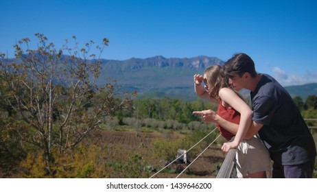 A Couple Is Standing On The Balcony Embracing. Look On The Trees Landscape - Sideview