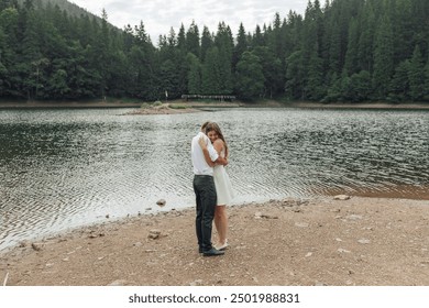 A couple is standing on a beach near a lake, hugging each other. The scene is peaceful and romantic, with the couple enjoying each other's company in a beautiful natural setting - Powered by Shutterstock