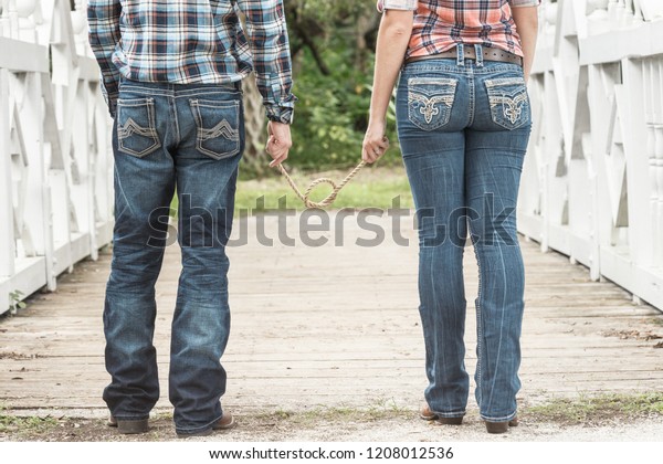 Couple standing on\
bridge facing away while holding a rope with a knot tied to signify\
marriage or engagement