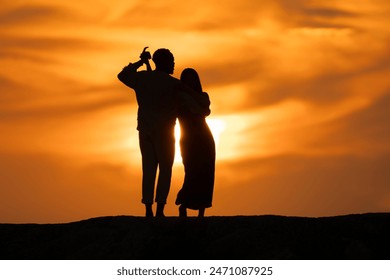 A couple standing on a hillside at sunset, with the woman hugging the man - Powered by Shutterstock