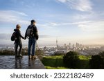 Couple standing on Mt Eden summit and watching sunrise over Auckland city. Selective focus on people in foreground. 