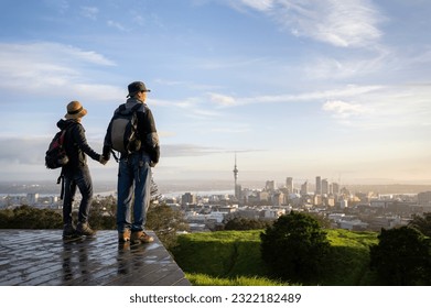 Couple standing on Mt Eden summit and watching sunrise over Auckland city. Selective focus on people in foreground. 