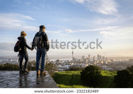 Couple standing on Mt Eden summit and watching sunrise over Auckland city. Selective focus on people in foreground. 