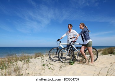 Couple standing on a sand dune with bicycles - Powered by Shutterstock