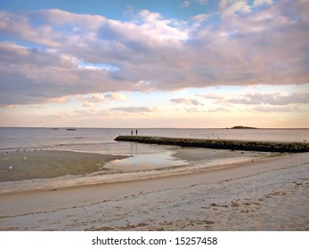 A Couple Is Standing On The Stone Jeddy During Low Tide At A Connecticut Beach.