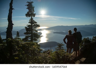 COUPLE STANDING On The Top Of Mountain Overlooking Islands During Sunset In Beautiful British Columbia Vancouver Canada After Hike In Forest 