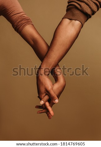 Couple standing side by side and holding hand with interlocked fingers. Cropped shot of two hands together showing unity.