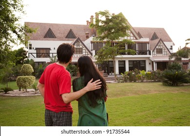 couple standing with their backs towards camera, couple standing against model house