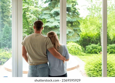 A couple standing at the window at home and looking out. Blond haired woman and grey hair man daydreaming. - Powered by Shutterstock