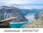 A couple stands on the edge of Trolltunga cliff in Norway, overlooking the stunning blue waters of a fjord. a couple of men and women on the edge of a mountain Trolltunga, Norway