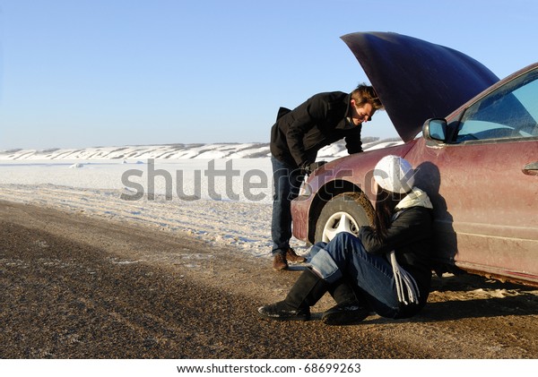 A couple are stranded at side of highway with a\
car breakdown in winter.