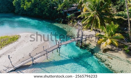 A couple strolls along a wooden bridge connecting lush greenery and pristine waters in Koh Kood, Thailand. The warm hues of dawn create a peaceful ambiance, inviting exploration and tranquility.