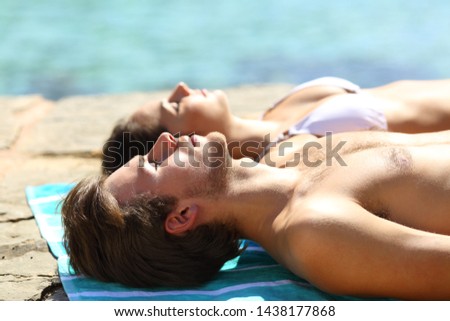 Couple sunbathing on summer vacation on the beach with the man in foreground