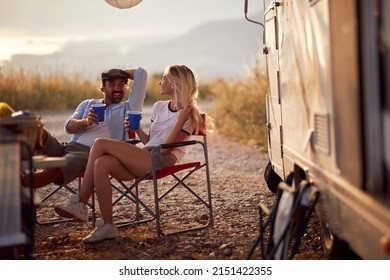 Couple at sunset cheering with drinks. Sitting in front of camper rv. Fun, togetherness, nature concept.