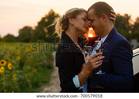 couple in the sunset, they are wearing smart casual clothes and drink champagne