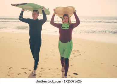 Couple with surfboards walking on beach. Front view of middle aged man and woman in wetsuits holding surfboards and walking on sea coast. Surfing concept - Powered by Shutterstock