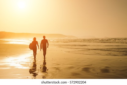 Couple of surfers leaving the water after surfing on a beautiful sunset at the beach. Body board and surf lifestyle concept. - Powered by Shutterstock