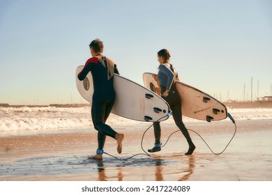 Couple of surfers with surfboards in wetsuit entering towards ocean for surfing on waves - Powered by Shutterstock