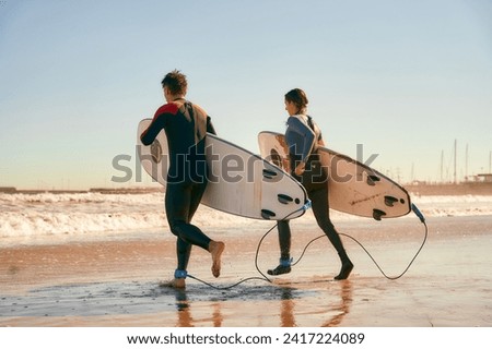 Couple of surfers with surfboards in wetsuit entering towards ocean for surfing on waves