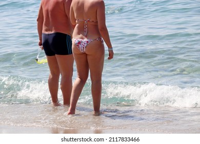 Couple In Swimwear Going To Swim In Sea Water, Rear View. Overweight Woman And Man With Snorkeling Mask On A Beach, Family Leisure