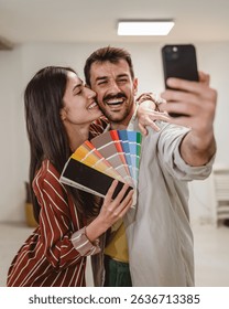 Couple take a self portrait while hold color palette and mobile phone choose new wall color