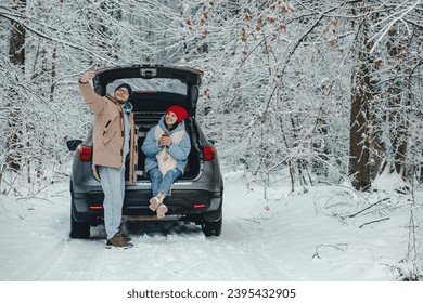 a couple takes a selfie next to their car in a snowy forest when they stop to take a break from the road and eat - Powered by Shutterstock