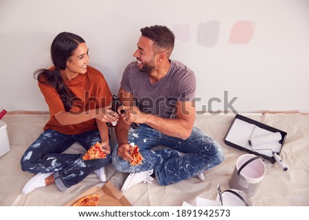 Couple Taking A Break And Drinking Beer And Eating Pizza As They Decorate Room In New Home Together