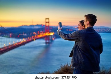 couple taking photo in front of golden gate bridge at sunrise shot with selective focus - Powered by Shutterstock