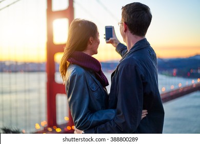 Couple Taking Selfie In Front Of Golden Gate Bridge At Sun Rise