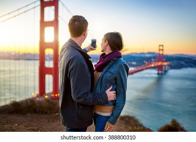 Couple Taking Selfie In Front Of Golden Gate Bridge At Sun Rise