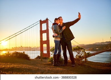 Couple Taking Selfie In Front Of Golden Gate Bridge At Sun Rise