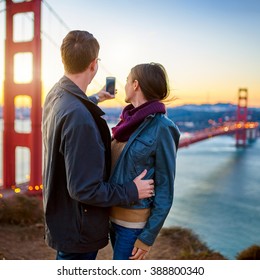 Couple Taking Selfie In Front Of Golden Gate Bridge At Sun Rise