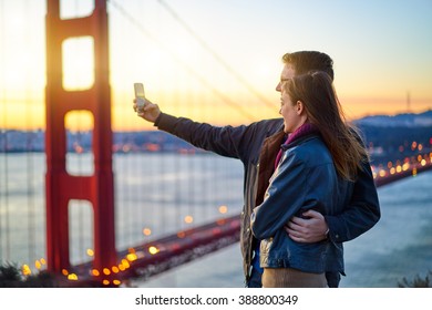 Couple Taking Selfie In Front Of Golden Gate Bridge At Sun Rise