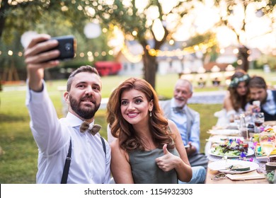 A Couple Taking Selfie At The Wedding Reception Outside In The Backyard.