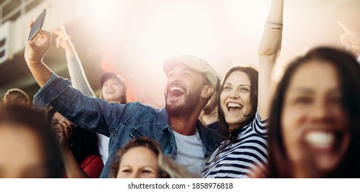 Couple taking selfie while cheering at stadium. Excited man and woman fans taking selfie while watching match in stadium. - Shutterstock ID 1858976818