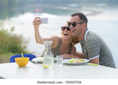 couple taking selfie while eating meal by water - Powered by Shutterstock