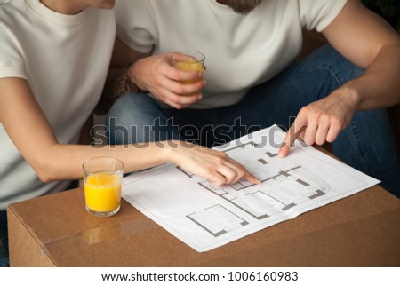 Couple talking about interior design with home plan, man and woman discuss renovation ideas pointing on blueprint holding orange juice, planning house remodeling apartment furnishing, close up view